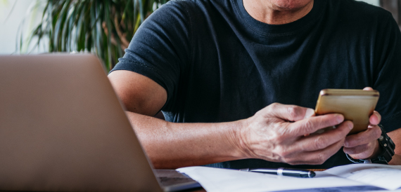 Man sitting at laptop using mobile phone